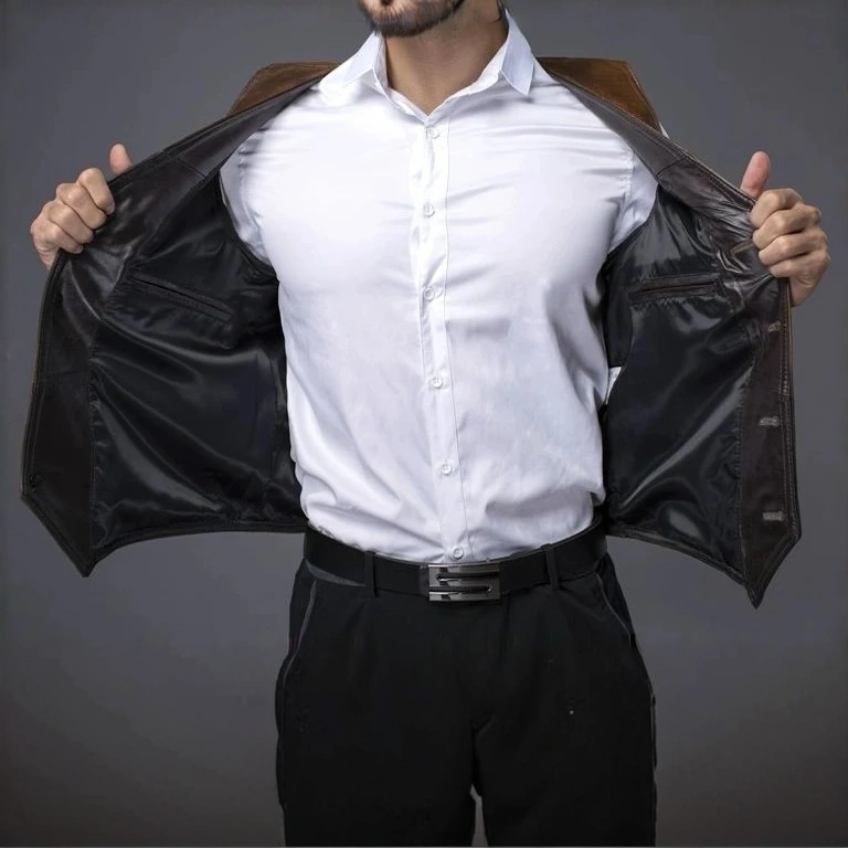 A man wearing a brown cowhide leather motorcycle vest on top of a white short sleeve polo shirt, showing the inside of the left and right sides of the vest and a pair of dark blue pants.