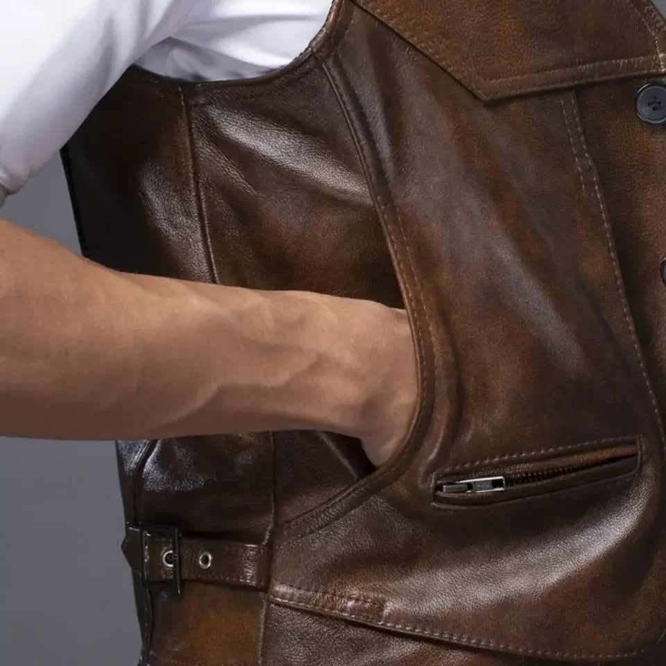 A man wearing a brown cowhide leather motorcycle vest on top of a white short sleeve polo shirt, with his hand inside the right side pocket.