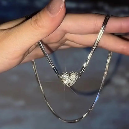 A woman's hand holding a silver chain with a silver broken heart rhinestone pendant.