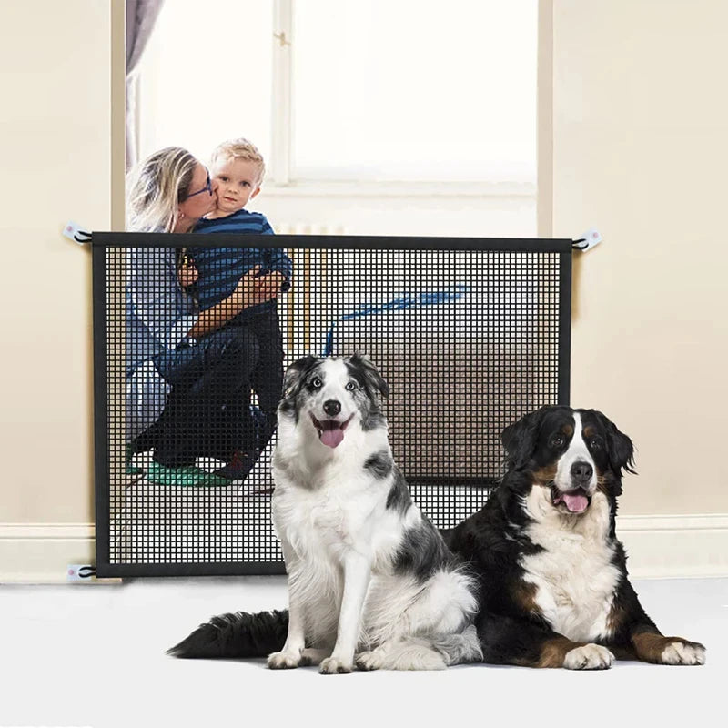 Two  dogs sitting in front of a mesh safety gate with a mother and child on the other side.