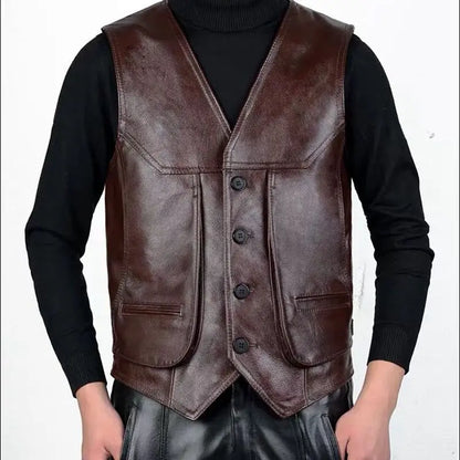 A man wearing a reddish brown cowhide leather motorcycle vest on top of a black turtleneck sweater, hands in pockets and a pair of black leather pants.