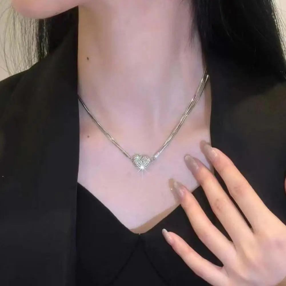 A woman wearing a silver chain with a broken heart rhinestone pendant, a v-neck and neckline showing.