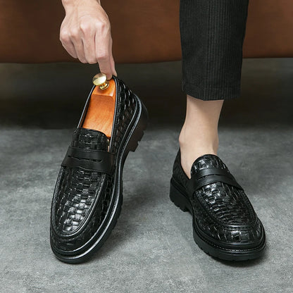 A man wearing one black woven loafer with black soles, holding the other one and with a pair of black corduroy pants .