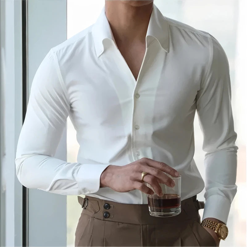 A man is wearing a white button down dress shirt and having a drink with brown pants on.