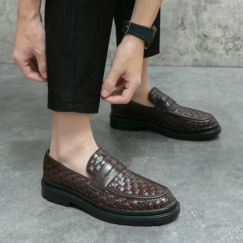 A man wearing a pair of brown woven loafers with black soles , no socks, a black watch and a pair of black corduroy pants.